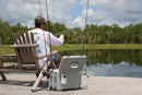 A man sitting on a dock fishing with his Engel Coolers Live Bait Pro cooler, rechargeable system by his side.