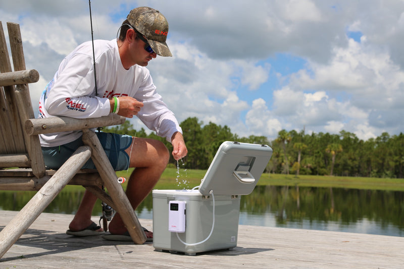 Sentence with replaced product name: A man sitting on a wooden bench near the Engel 13Qt Live bait Pro Cooler with AP3 Rechargeable Aerator & Stainless Hardware.