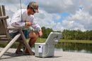 A man sitting on a wooden bench next to an Engel Coolers 19Qt Live bait Pro Cooler with AP3 Rechargeable Aerator & Stainless Hardware.