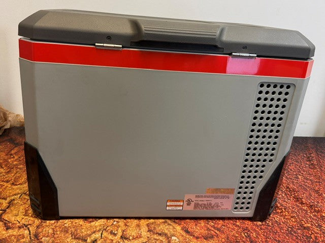 A gray and black Engel MR040 Top Opening Fridge-Freezer from Engel Coolers, featuring a red stripe and ventilation holes, sits on a brown textured surface—highlighting its corrosion-resistant design that's perfect for marine environments and serves as an excellent portable cooling solution.