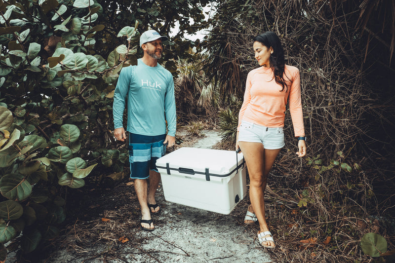 A man and woman walking down a path with an Engel Coolers ENGEL 60QT UltraLite Injection-Molded Cooler With Wire Basket and Divider.