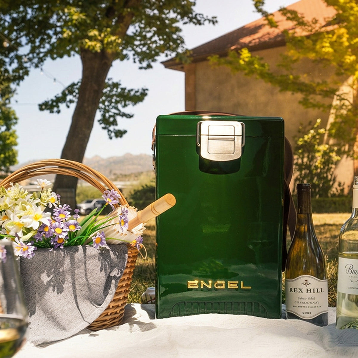 Dark green Engel Reserve Premium Wine Cooler sitting on a picnic blanket next to a basket of flowers and two bottles of wine.