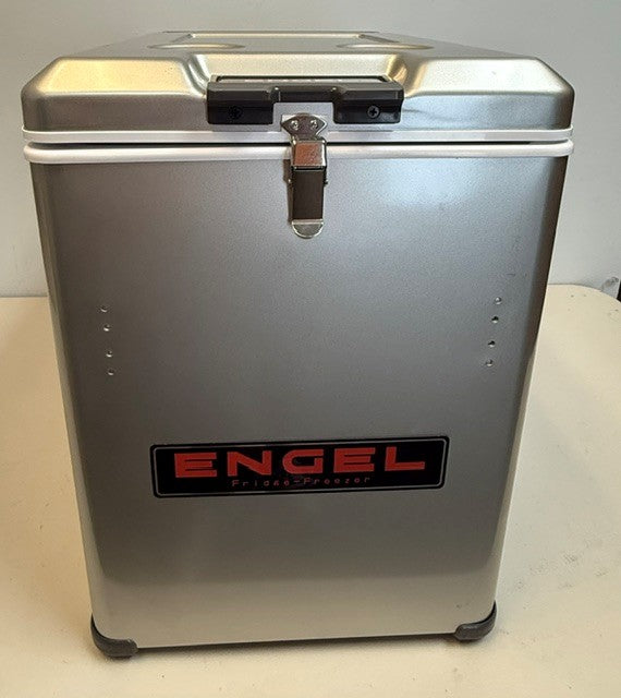 An Engel Coolers MT45 Combination Platinum Series Top Opening 12/24V DC -110/120V AC Fridge-Freezer sits on a white surface against a plain background. This silver unit, adorned with a black and red Engel logo on the front and secured by a sturdy metal latch, features the innovative Swing Motor Compressor to provide reliable cooling and freezing on the go.