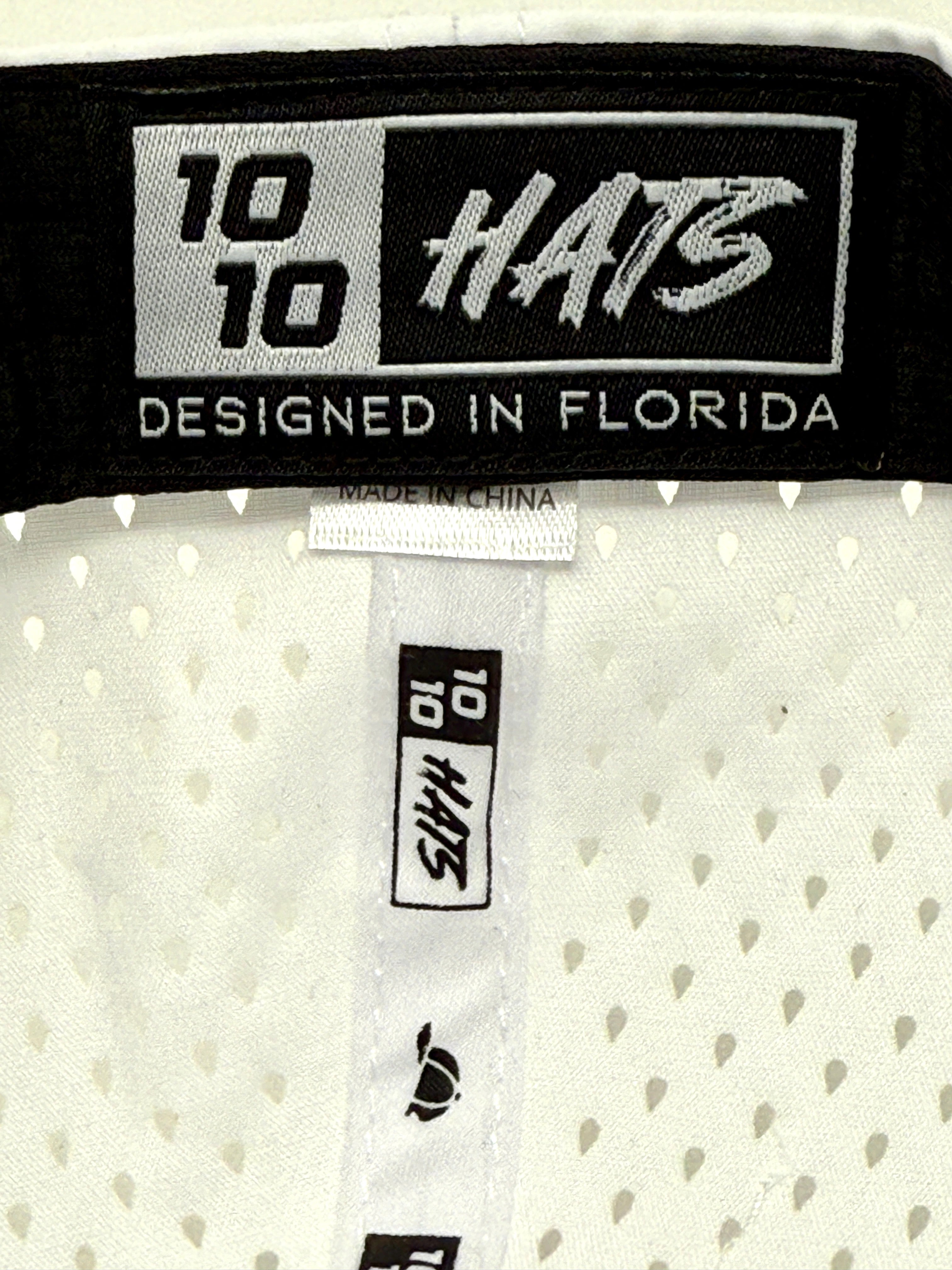 Close-up of inside labels on the Engel 1010 Performance Trucker Cap by Engel Coolers, blue with white logo, showing “DESIGNED IN FLORIDA” and “MADE IN CHINA” tags on perforated white mesh fabric.