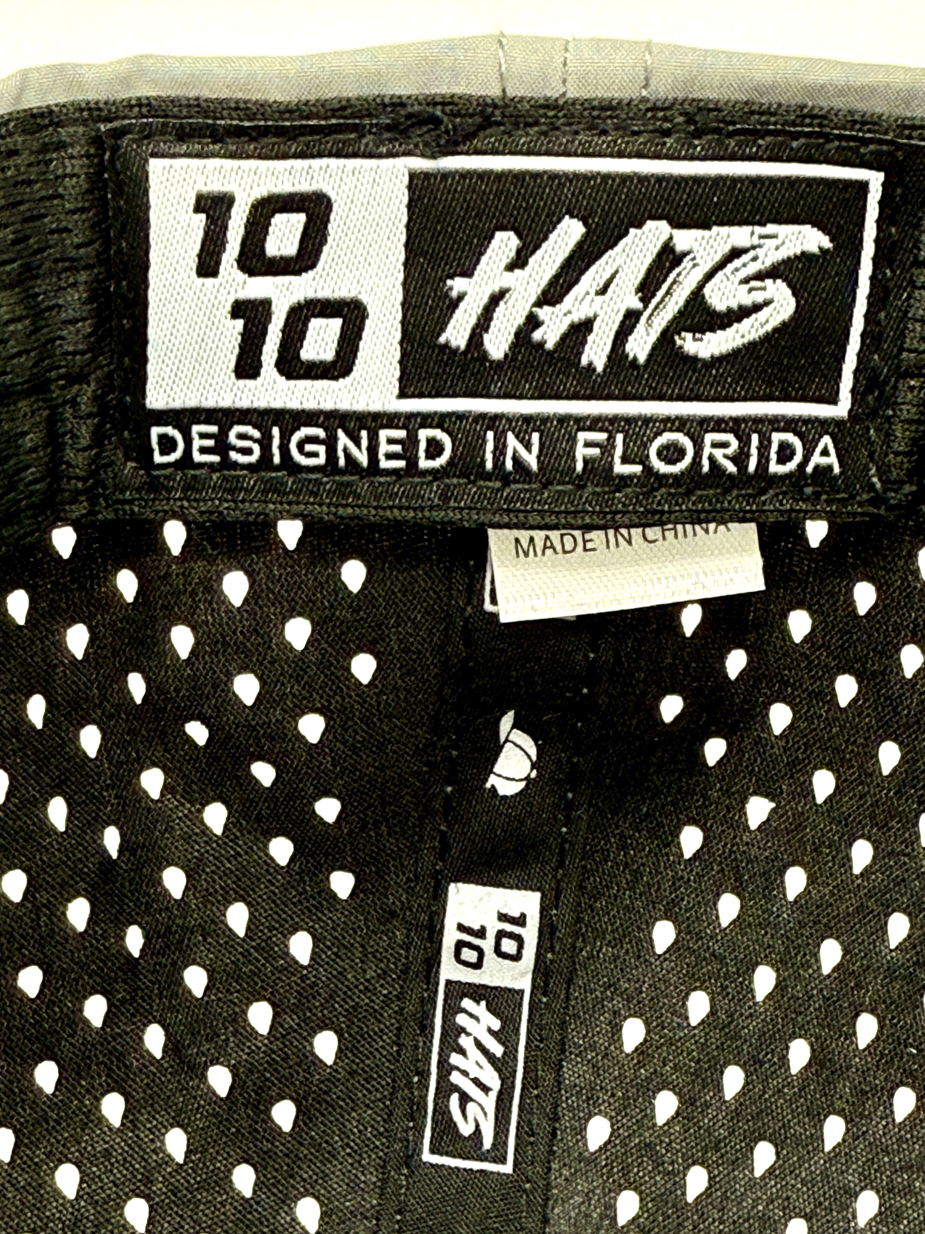Close-up of hat labels reading "Engel Coolers 1010 Performance Trucker Cap Designed in Florida" and "Made in China" on black breathable mesh, highlighting the signature style of Engel Coolers' performance caps.