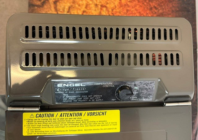 Close-up of the Engel Coolers MT27 fridge-freezer control panel, featuring the temperature control dial and a caution label in English, French, and German. The image highlights the reliable Swing Motor compressor technology that makes this portable fridge freezer from Engel Coolers ideal for travel.