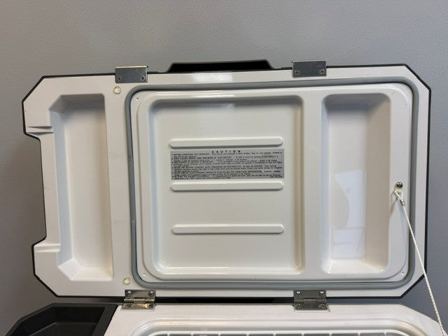 The Engel MR040 Top Opening Fridge-Freezer by Engel Coolers is shown open against a plain gray wall, displaying its white, corrosion-resistant ABS case ideal for marine environments, with a hinged lid that reveals two rectangular recessed areas and a visible caution label on the inside.