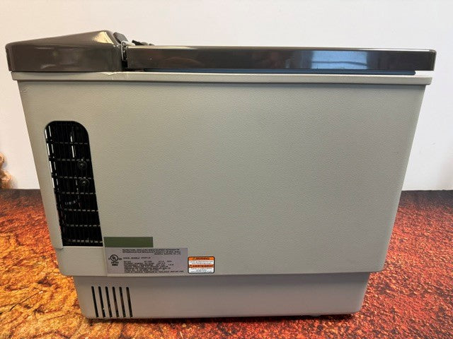 The Engel MT27 by Engel Coolers is a gray portable electric cooler featuring a closed dark gray lid and a black vent on the left side, shown resting on a reddish-brown surface against a plain background; this compact fridge-freezer utilizes dependable Swing Motor compressor technology to deliver efficient cooling wherever you need it.