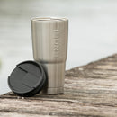 A stainless steel, vacuum-insulated 22oz Maverick Tumbler with a lid next to a body of water.