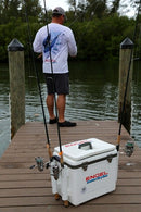 A man standing on a dock, with two fishing rods and an Engel Cooler Cushion for 30 Quart Drybox or Live Bait Cooler beside him.