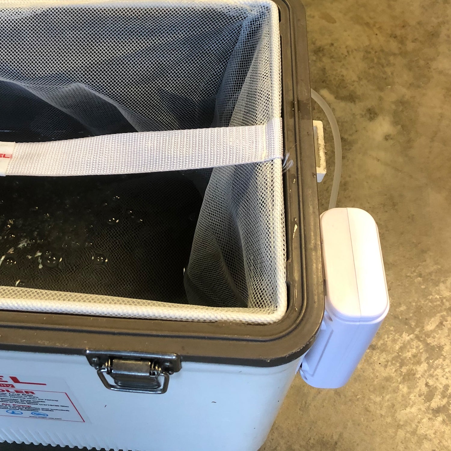 A white Engel cooler with a mesh bag inside.
Replace with:
A white Engel Coolers Lithium-ion Rechargeable Live Bait Aerator Pump cooler with a mesh bag inside.