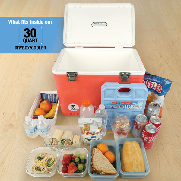 An open Engel Coolers Engel 30 Quart Drybox/Cooler sits on a wooden floor, displaying sandwiches, wraps, fruit, bottled water, soda cans, snacks, and a large ice pack.