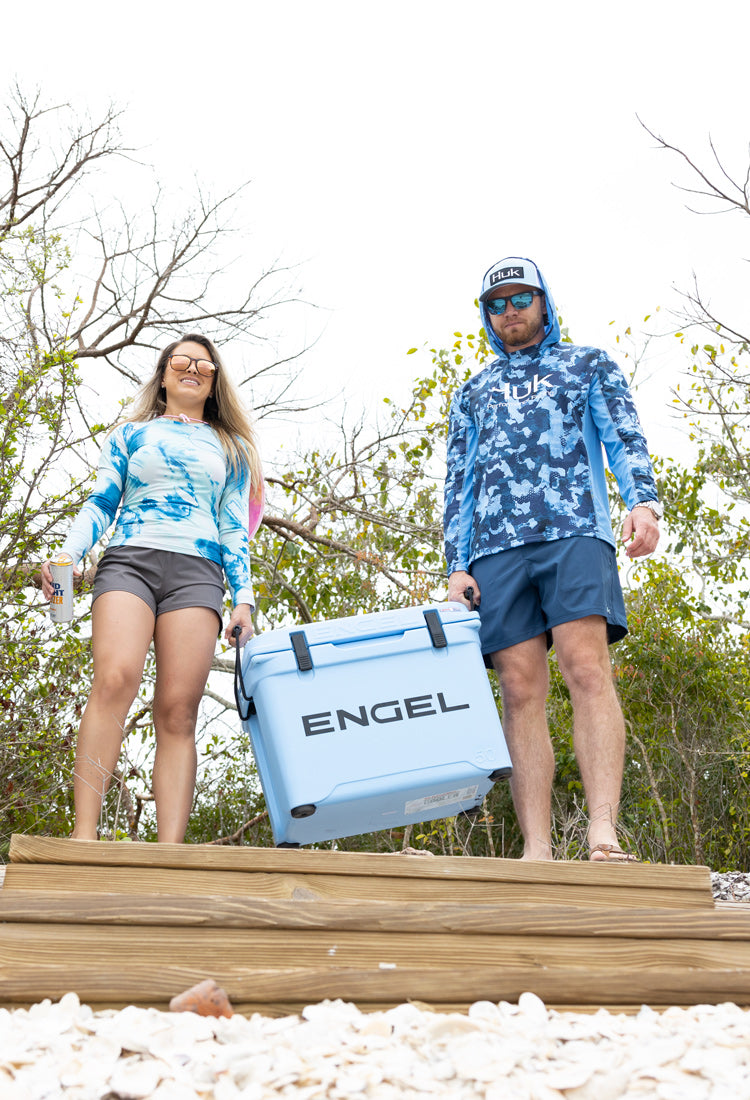 A man and woman standing next to a cooler on a beach.