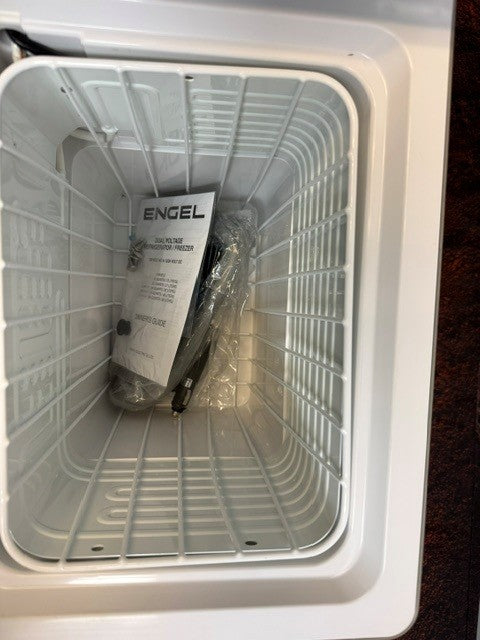 Open white Engel Coolers MT27 fridge-freezer with instruction manual, plastic packaging, and a power cord inside. The ribbed interior walls are empty except for these items, highlighting the efficient design typical of a portable fridge freezer featuring Engel’s Swing Motor compressor.
