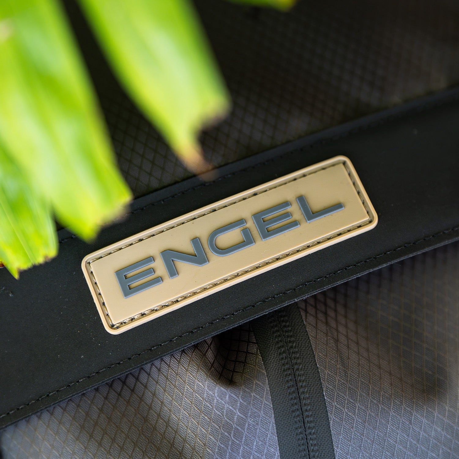 Close-up of the ENGEL GoBag 20 Qt Backpack Day Bag featuring a stitched beige “ENGEL” label; part of a green plant appears in the upper left corner.