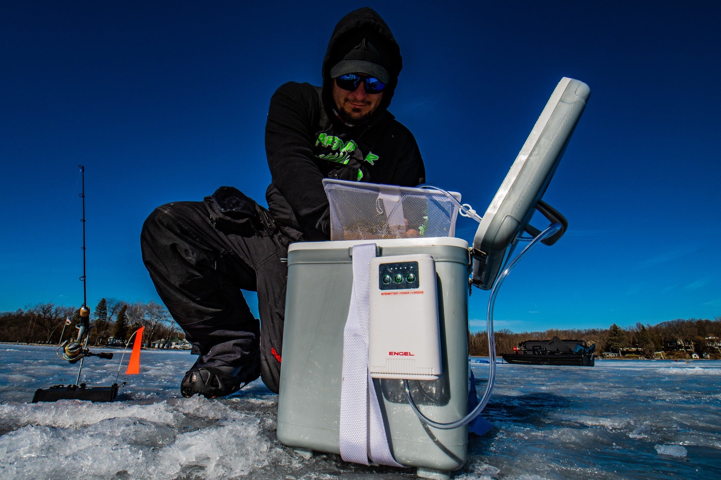 A man holding an Engel Coolers 13Qt Live bait Pro Cooler equipped with a rechargeable aerator for the live bait storage system on the ice.