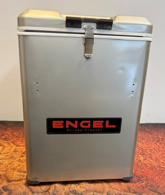 An Engel Coolers MT45 Platinum Series portable fridge-freezer in silver, distinguished by its black and red logo, rests on a textured surface secured with a latch and white strap. Famous for its efficient Swing Motor Compressor, this unit is engineered for durability and advanced cooling performance.