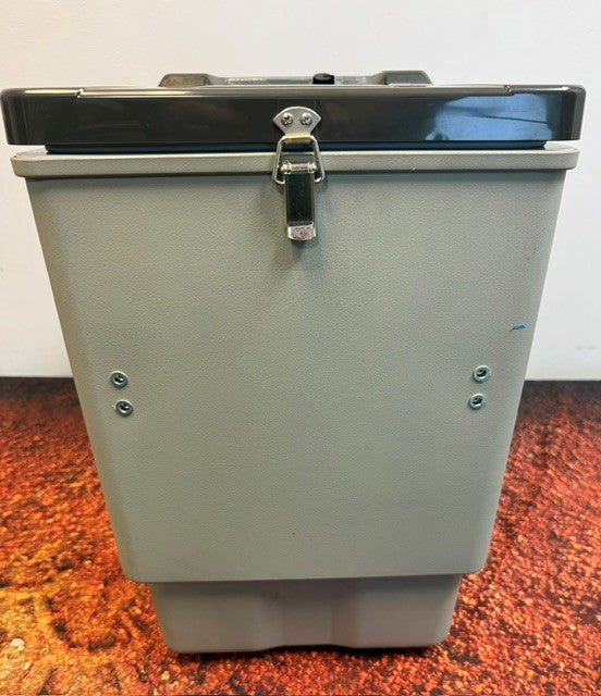An Engel Coolers Engel MT27, a gray metal box featuring a latch on top and screws on the front, is positioned on a reddish speckled surface against a white background.