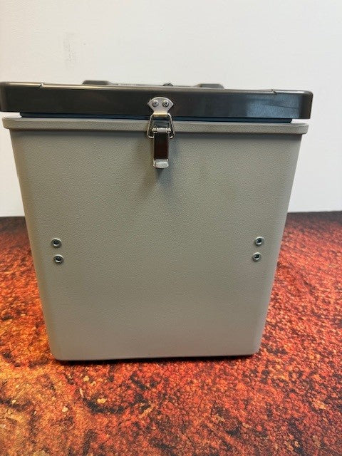 An Engel Coolers MT17F top-opening 12/24V DC - 110V/120V AC fridge-freezer, a gray and black rectangular metal box with a top latch, sits on a reddish-brown speckled surface against a white wall.