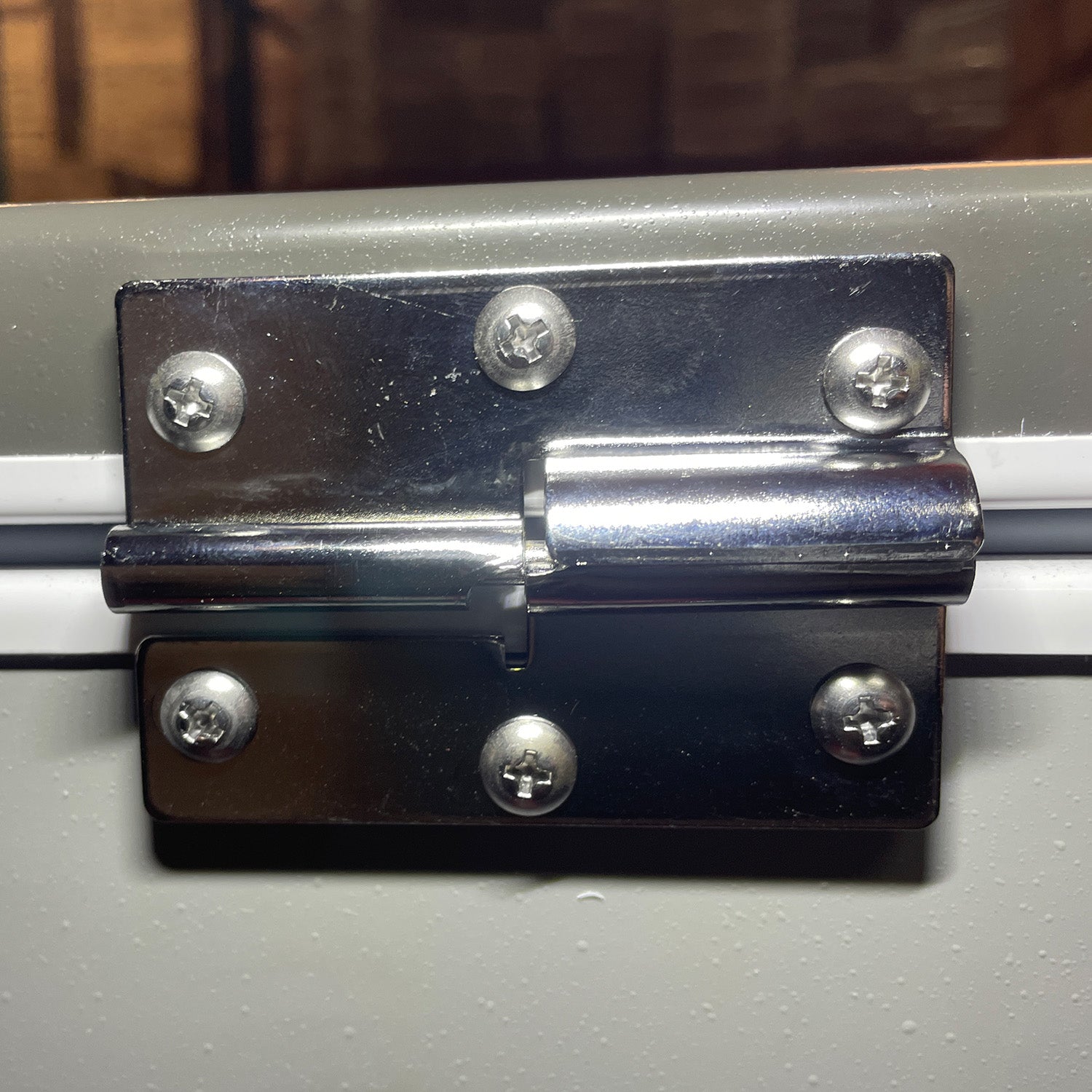 Close-up of an Engel Coolers MT60/80 Reverse Hinge set securely fastened with six screws on a gray painted surface.