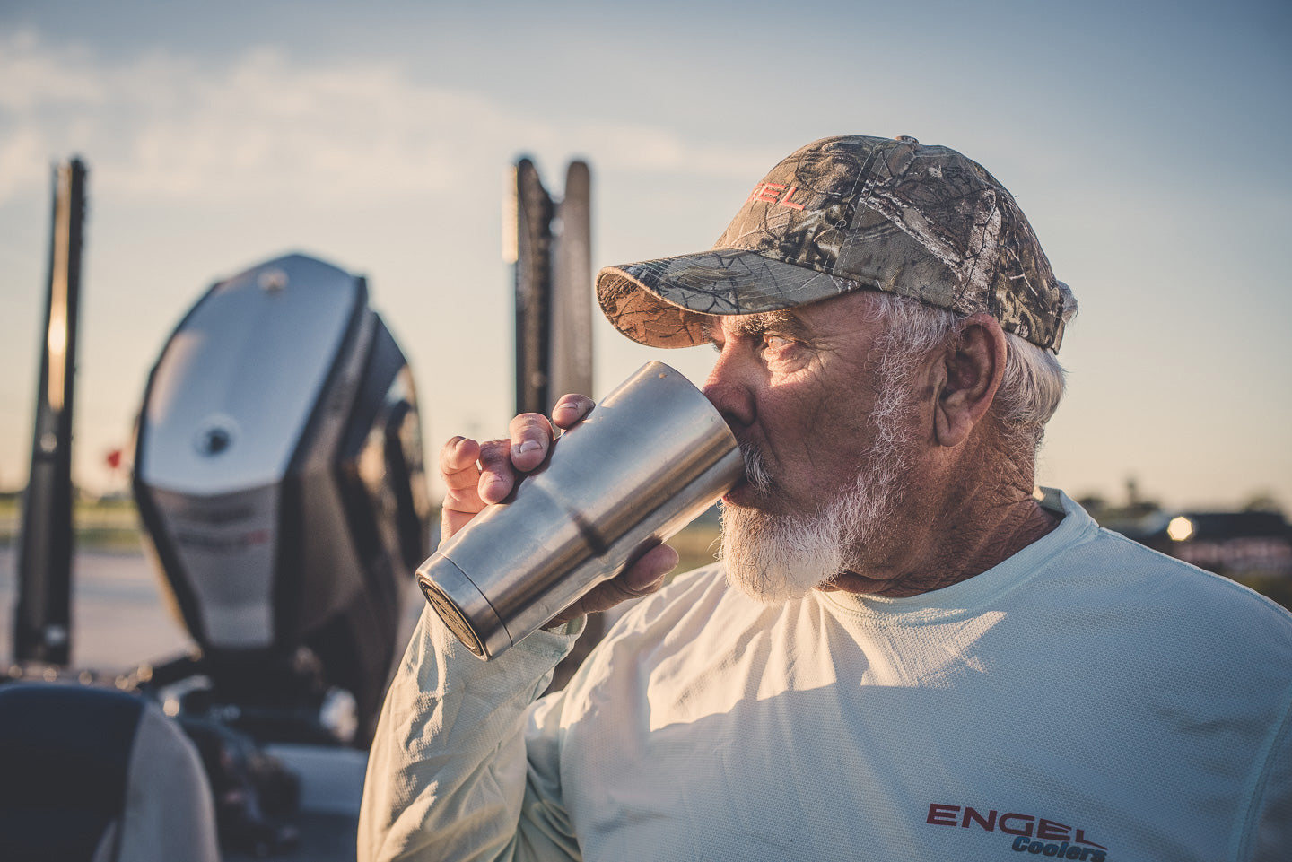 An older man in a cap enjoys a refreshing drink from his Engel Coolers 22oz Stainless Steel Vacuum Insulated Tumbler, part of the Color Collection, while standing outdoors near a vehicle.