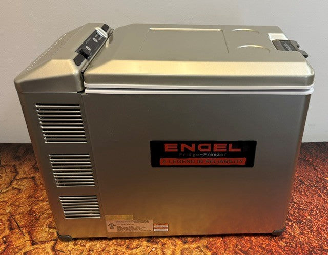 An Engel Coolers MT45 Platinum Series portable fridge-freezer rests on a textured surface, showcasing vents, control knobs, and a distinctive logo on its side. This model is equipped with a Swing Motor Compressor for dependable performance in any environment.
