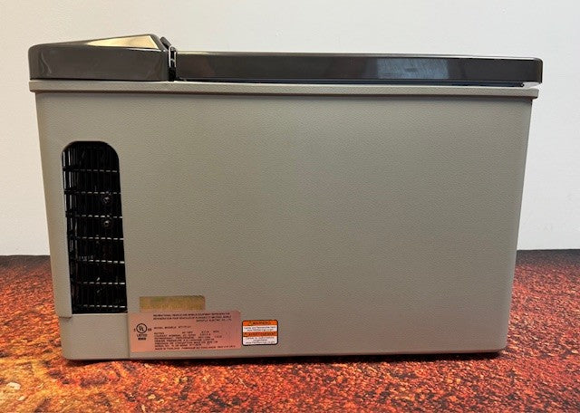 An Engel Coolers MT17F top-opening fridge-freezer with a black side vent and safety labels sits on a reddish-brown surface against a white wall; it features a swing motor compressor and supports 12/24V DC or 110/120V AC.