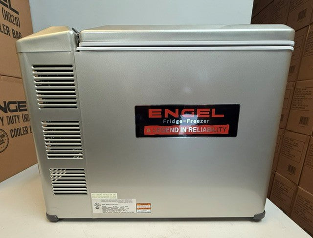 A refurbished Engel MT45 Platinum Series fridge-freezer from Engel Coolers, featuring a silver finish and a black and red label, sits on a flat surface with cardboard boxes in the background.