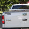 A white Ford F-150 truck with a removable 7.5" ENGEL COOLERS Window Decal in Black or Red and Blue decal on the tailgate is parked on a sunlit street lined with trees.