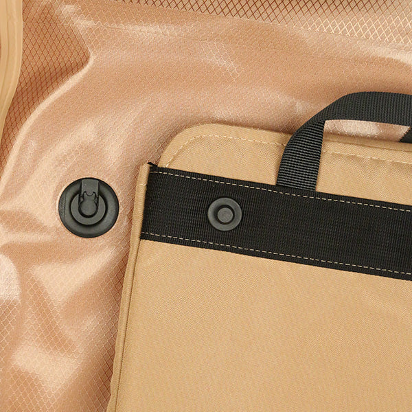 Close-up of a tan fabric strap with a black button snap and handle, attached to a beige textured surface with a black plastic valve—part of the ENGEL GoBag 20 Qt Backpack Day Bag, an ultra-light, waterproof backpack designed by ENGEL for adventure and convenience.