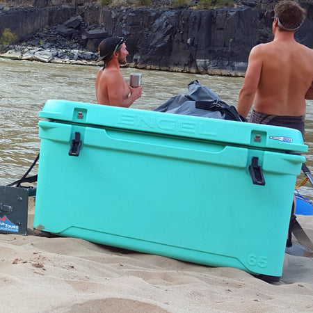 Two men standing in the sand next to a cooler.