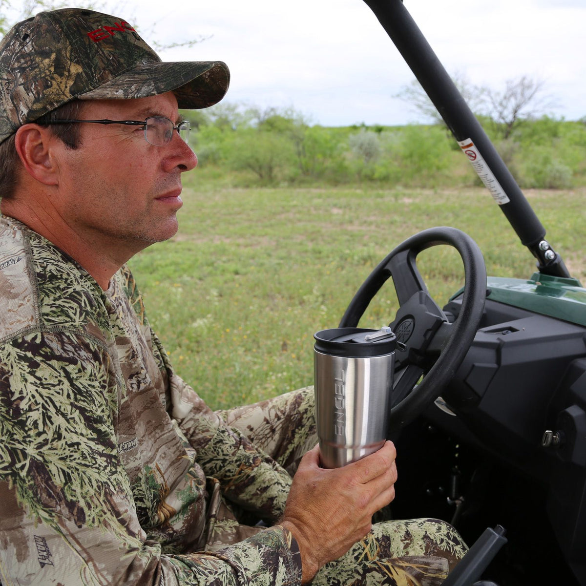 A man in a camouflage shirt holding an Engel 30oz Black Stainless Steel Tumbler by Engel Coolers.