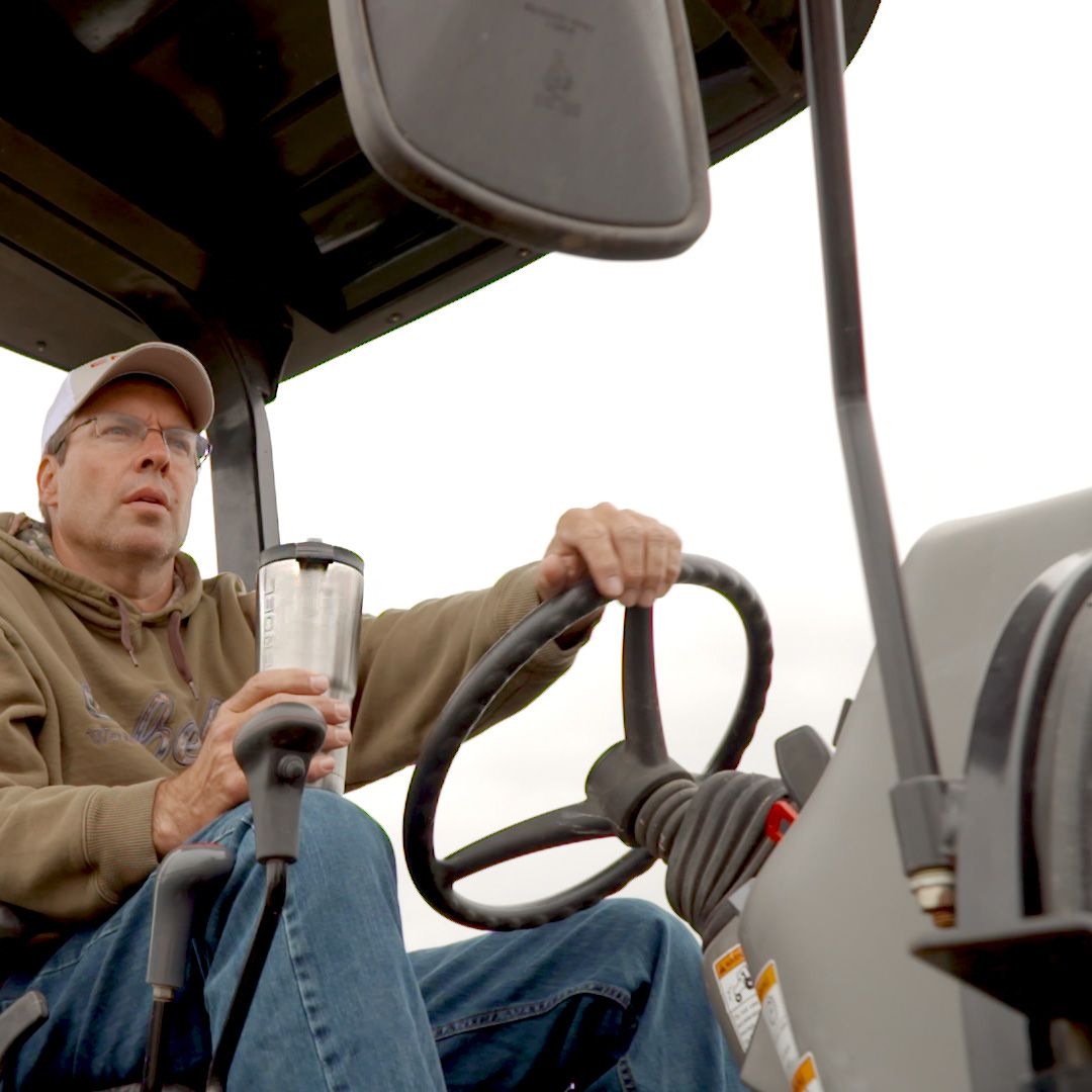 A man driving a tractor holds an Engel Coolers 30oz Stainless Steel Vacuum Insulated Tumbler.